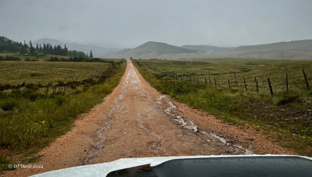 Photograph through a windshield of driving down a dirt road in a rain storm